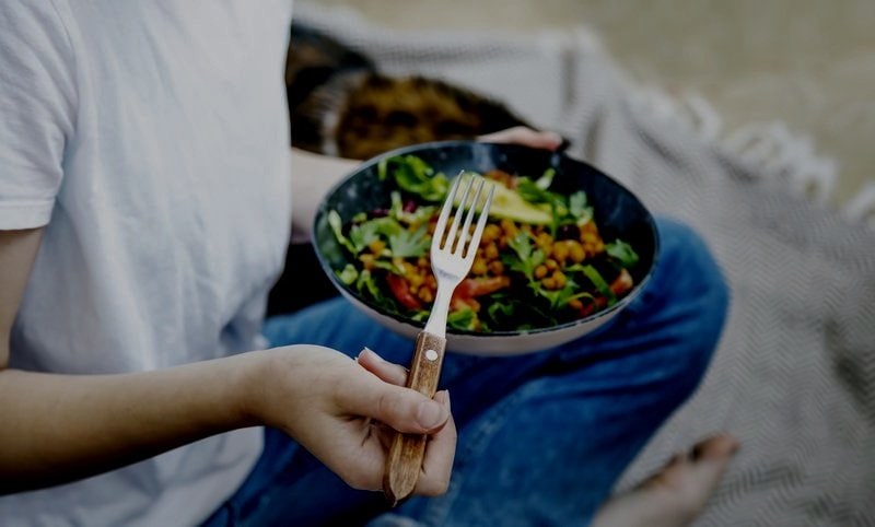 Man sitting outside on a blanket while holding a bowl of organic food - MosaicDX